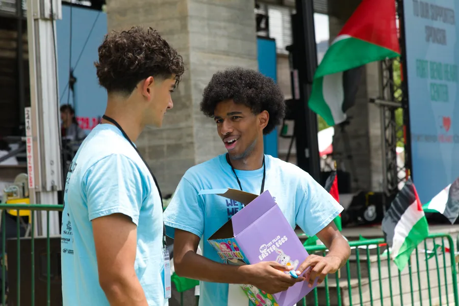 Two young people in festival shirts speaking beside Palestinian flags