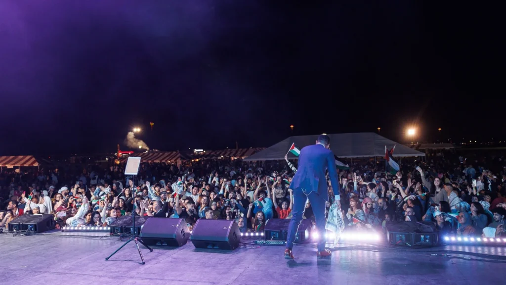 A performer facing a large Houston Palestinian Festival crowd waving Palestinian flags