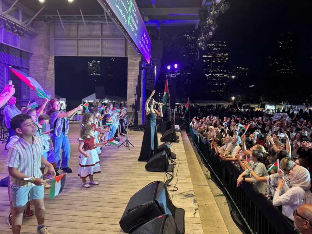 Children and adults waving Palestinian flags onstage beside a singer and the festival audience.