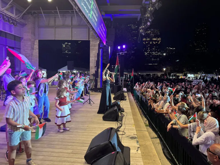 Children and adults waving Palestinian flags onstage beside a singer and the festival audience.