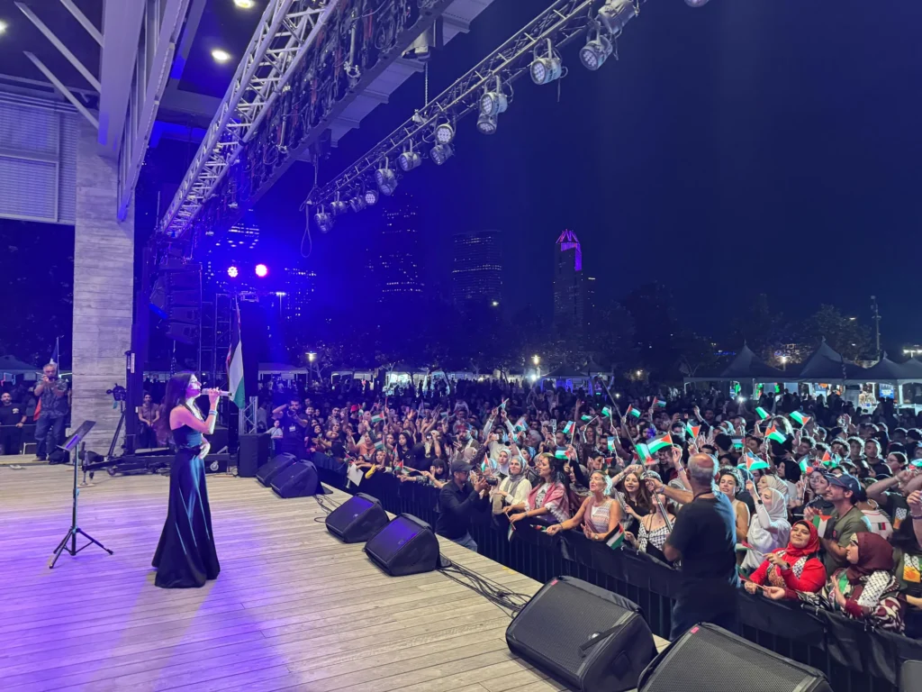 A singer performing onstage beside an audience waving Palestinian flags at night.